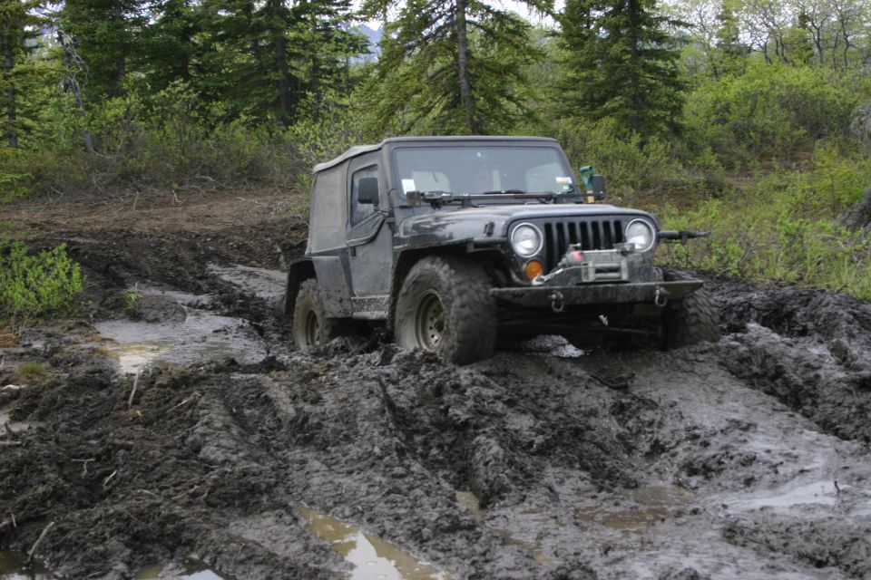 2003 Jeep TJ navigating a muddy trail with trees in the background