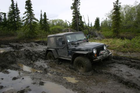 2003 Jeep TJ - A black Jeep Wrangler TJ is stuck in thick mud on a trail surrounded by trees.