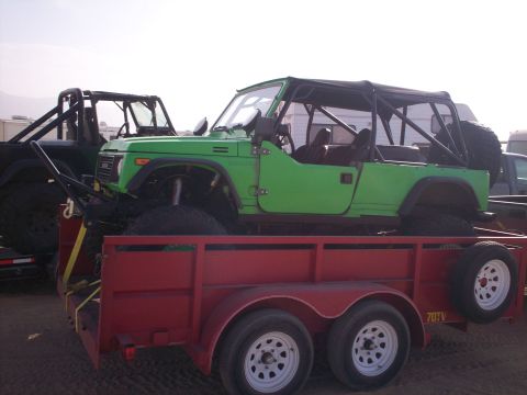 1987 Suzuki Samurai - A modified green 1987 Suzuki Samurai is transported on a red trailer, accompanied by another off-road vehicle.