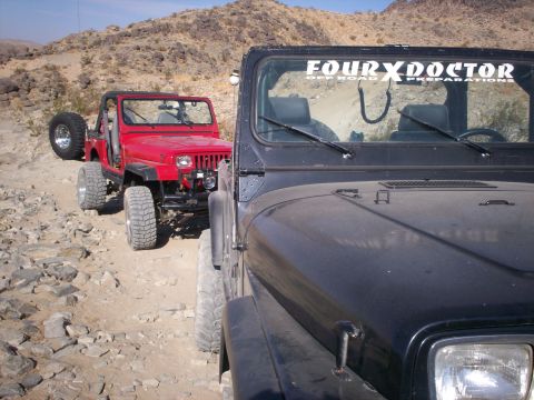 1987 Suzuki Samurai - Two Jeeps navigate a rocky desert trail under a clear blue sky.