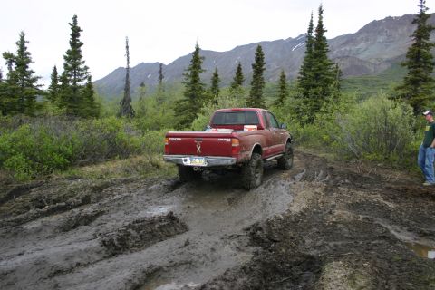 2003 Jeep TJ - A red Toyota Tacoma navigates a muddy trail with mountains in the distance.