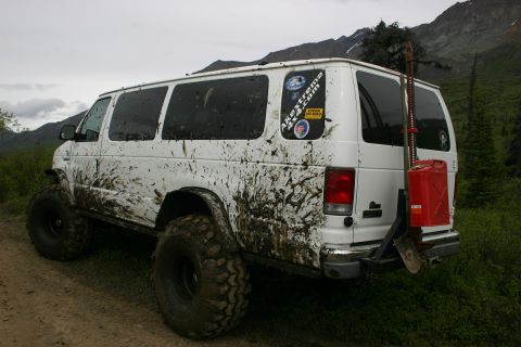 2003 Jeep TJ - Muddy van with off-road modifications parked on a dirt road with mountains in the background.