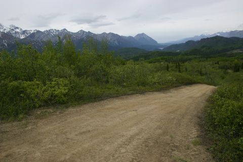 2003 Jeep TJ - A dirt road winds through lush greenery towards a distant valley and mountains under a cloudy sky.
