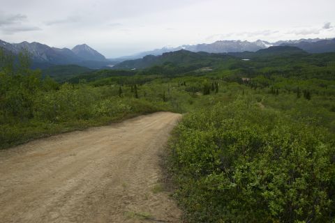 2003 Jeep TJ - A dirt road winds through a lush green landscape towards distant, hazy mountains.