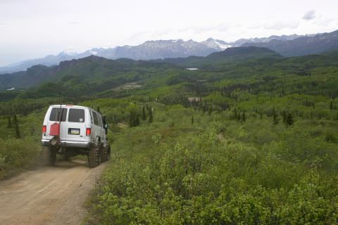 2003 Jeep TJ - A modified van navigates a dirt path through a lush, mountainous landscape.
