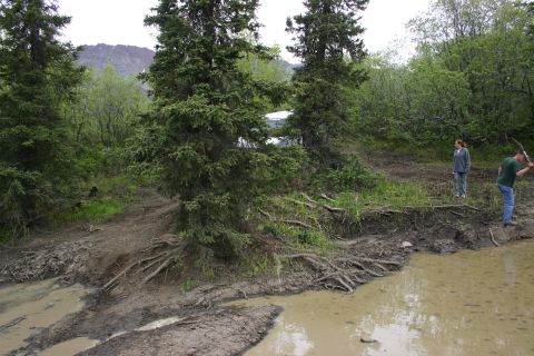 2003 Jeep TJ - Two people observe a muddy off-road area with trees and a pond.