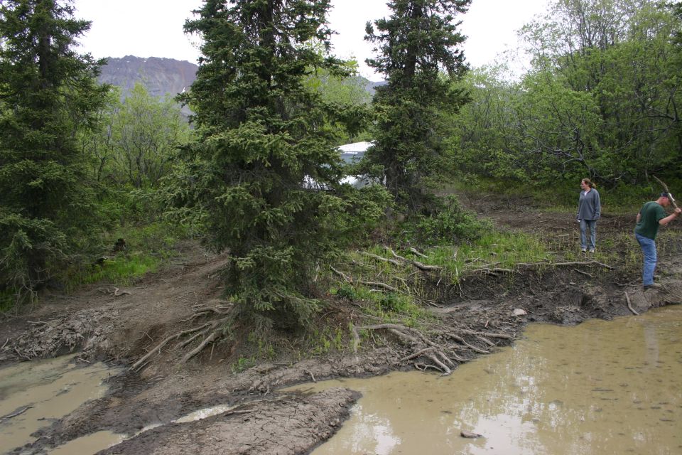 Muddy trail next to a pond with two people standing on the bank