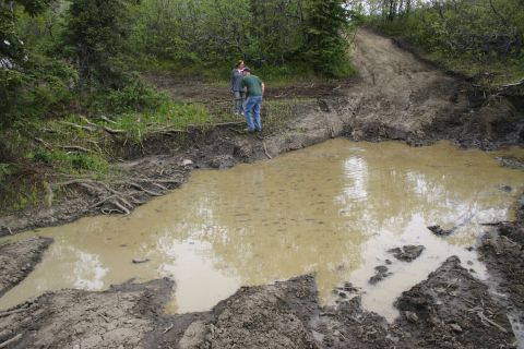 2003 Jeep TJ - Two people observe a challenging muddy off-road path with a large water-filled pothole.