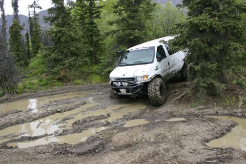 2003 Jeep TJ - Modified white van navigates a muddy trail in a wooded area.