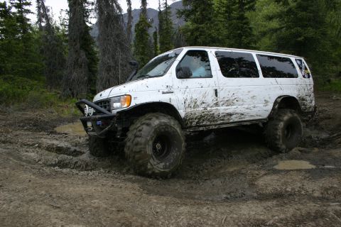2003 Jeep TJ - A white van navigates a muddy off-road trail with large tires and an aftermarket bumper.