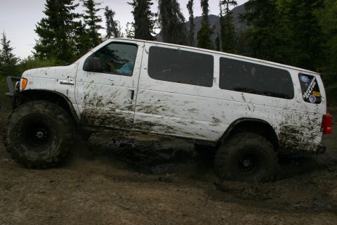 2003 Jeep TJ - This white van, heavily caked in mud, navigates a challenging off-road terrain with its oversized tires.