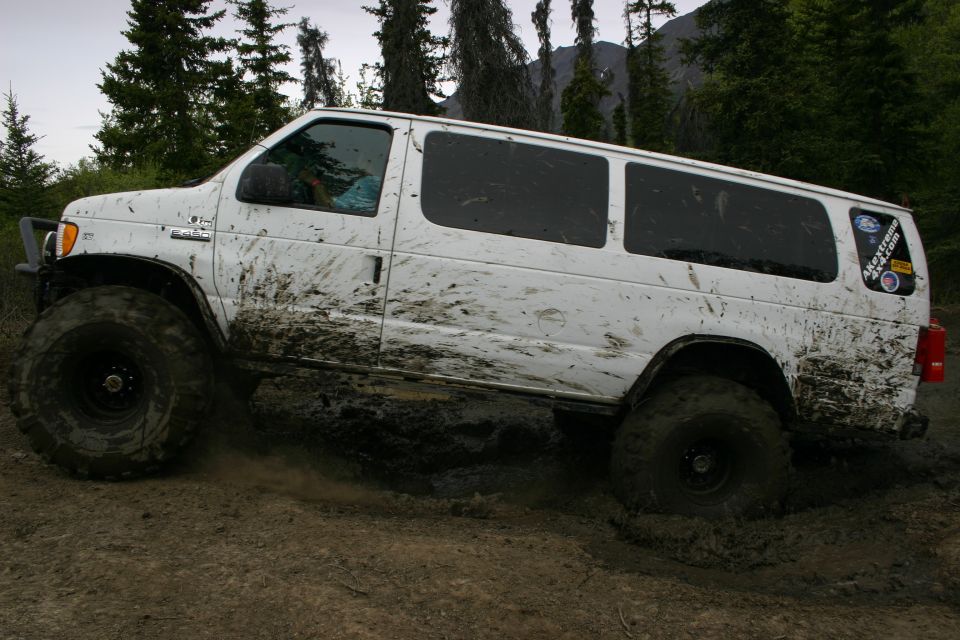 White van with large tires driving through mud, covered in mud