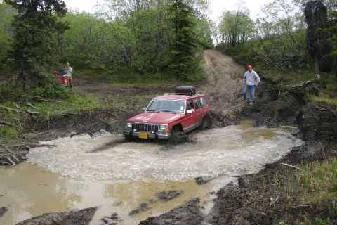 2003 Jeep TJ - A red Jeep Cherokee XJ navigates a challenging muddy off-road course.