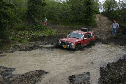 2003 Jeep TJ - A red Jeep Cherokee XJ navigates a muddy trail during an off-road event.
