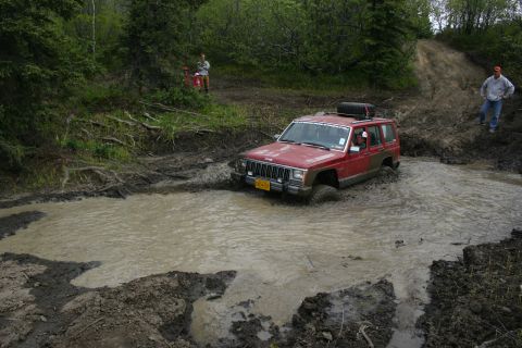 2003 Jeep TJ - A red Jeep Cherokee XJ navigates a muddy obstacle on an off-road trail.