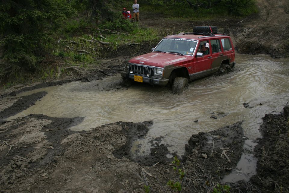 red Jeep Cherokee XJ driving through a muddy water obstacle