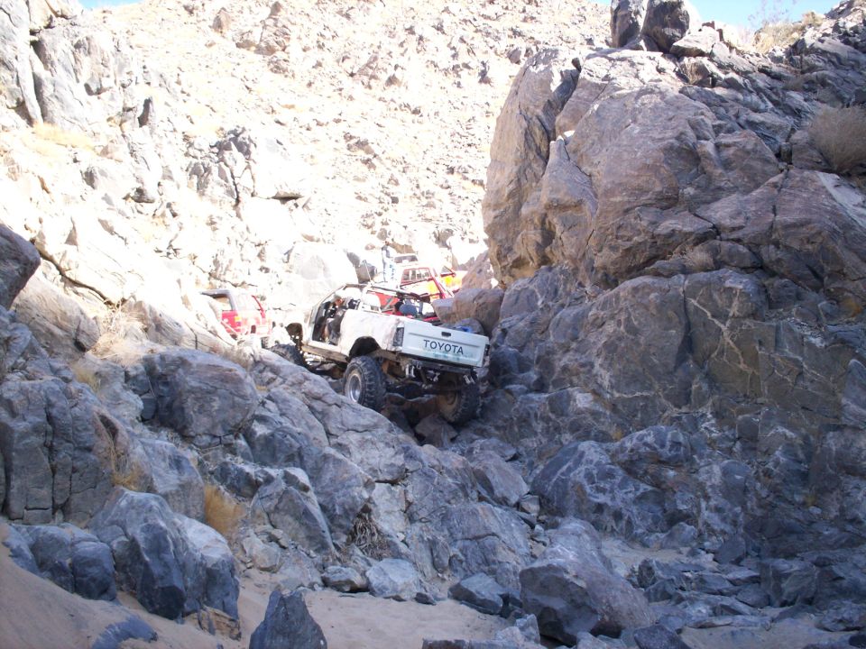 Toyota pickup truck navigating a rocky, off-road trail. Another vehicle is visible behind it