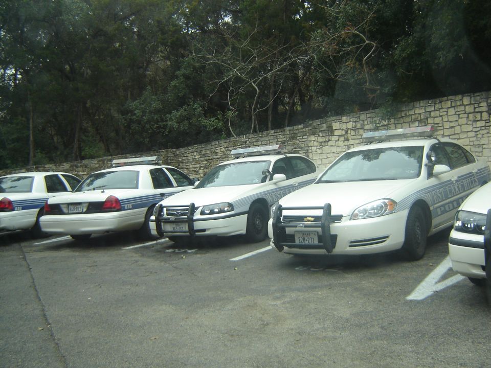 Several white police cars parked in a lot. One has "WEST LAKE HILLS POLICE" on the side