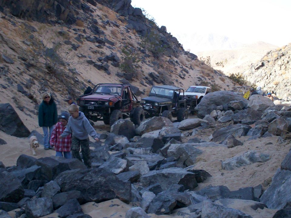 Several off-road vehicles navigate a rocky, sandy trail in a desert canyon