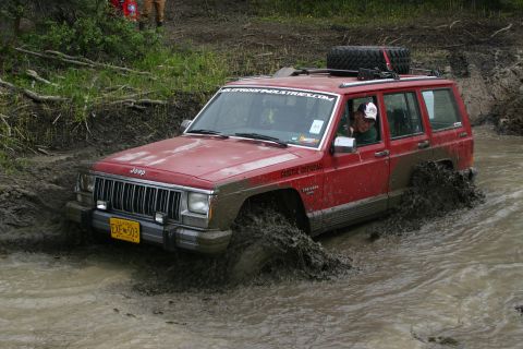 2003 Jeep TJ - Jeep Cherokee XJ navigates a muddy trail, kicking up water and dirt.