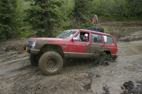 2003 Jeep TJ - Off-roading in the mud with a Jeep Cherokee XJ, another vehicle and people are visible in the background.