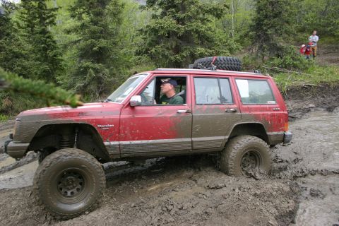 2003 Jeep TJ - Jeep Cherokee XJ navigating a muddy off-road trail with a driver inside.