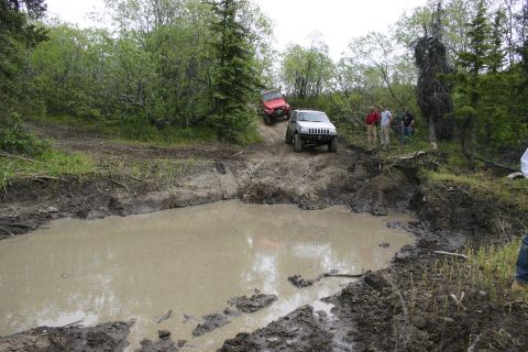 2003 Jeep TJ - Two off-road vehicles tackle a challenging muddy course with spectators observing the action.