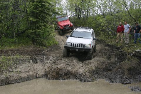 2003 Jeep TJ - Two Jeeps tackle a challenging muddy off-road course with onlookers watching.