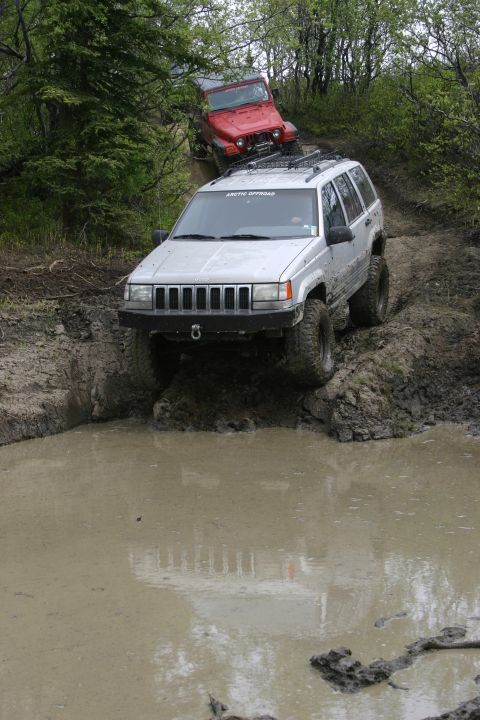 2003 Jeep TJ - A silver Jeep Grand Cherokee navigates a muddy trail, with a red Jeep Wrangler following closely behind.