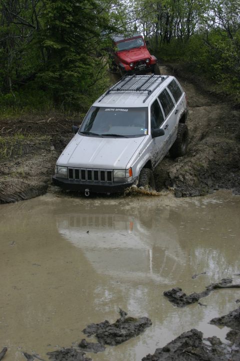 2003 Jeep TJ - Two Jeeps navigating a muddy trail, with the silver Grand Cherokee partially submerged in water.