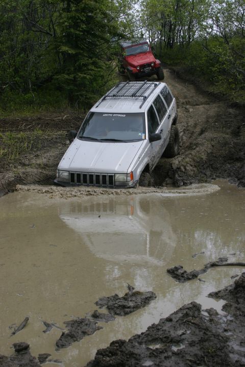2003 Jeep TJ - Two off-road vehicles navigate a challenging muddy terrain, with one SUV deeply mired in a water-filled rut.