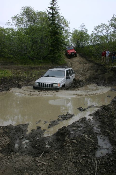 2003 Jeep TJ - A silver Jeep Grand Cherokee is stuck in a deep mud pit while another Jeep navigates a muddy hill.
