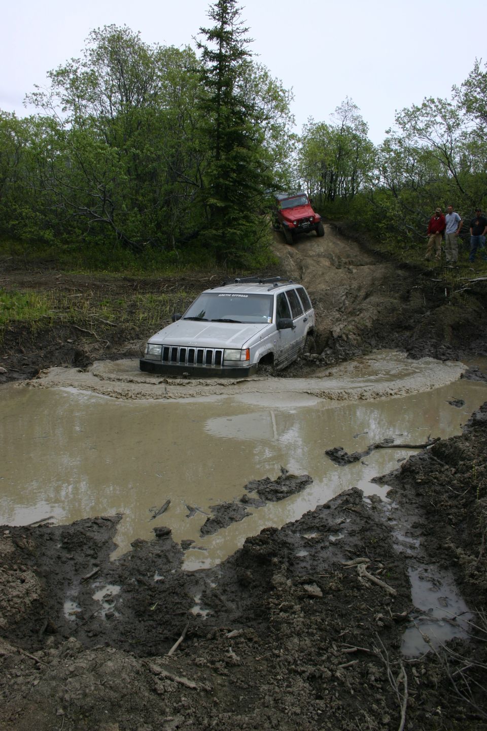Silver Jeep Grand Cherokee stuck in a mud pit, front grille visible