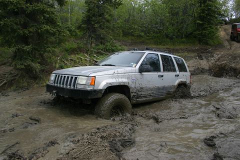 2003 Jeep TJ - A Jeep Grand Cherokee navigates a muddy trail, with another vehicle following behind.