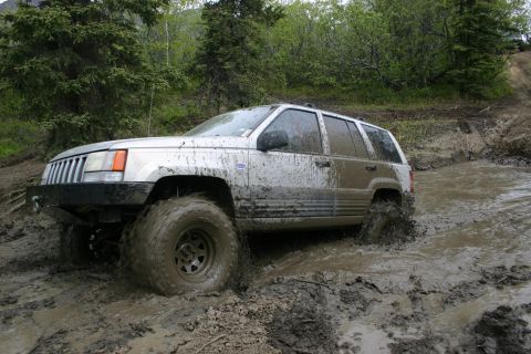 2003 Jeep TJ - A silver SUV navigates a muddy trail, kicking up water and mud.