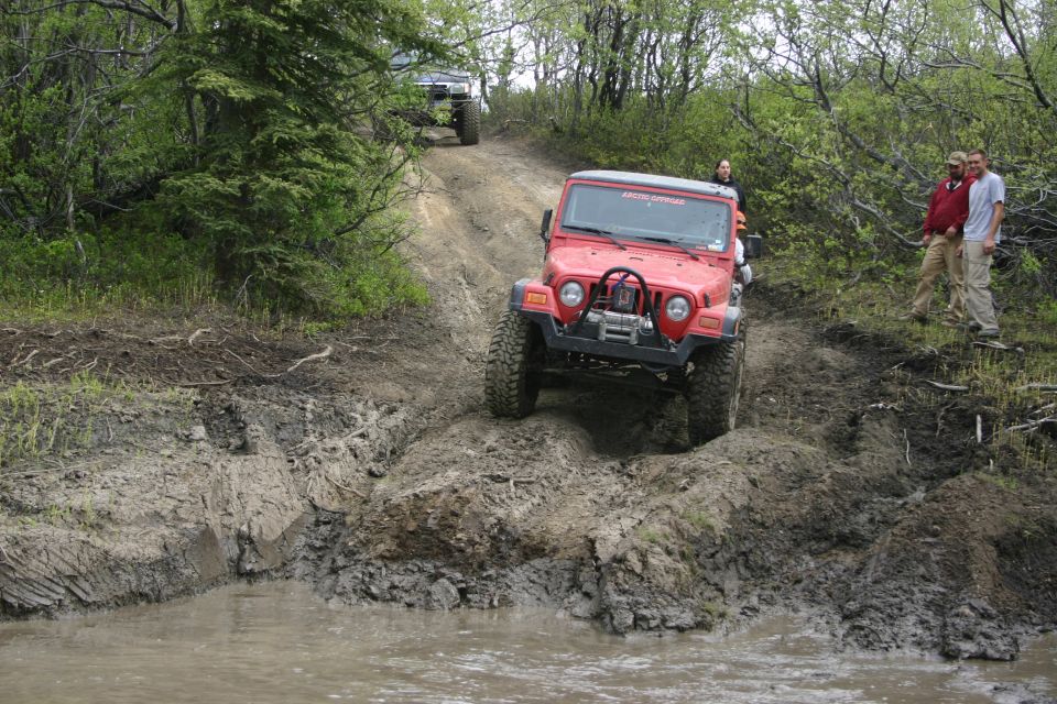 Red 2003 Jeep TJ navigating a muddy trail with another Jeep behind it