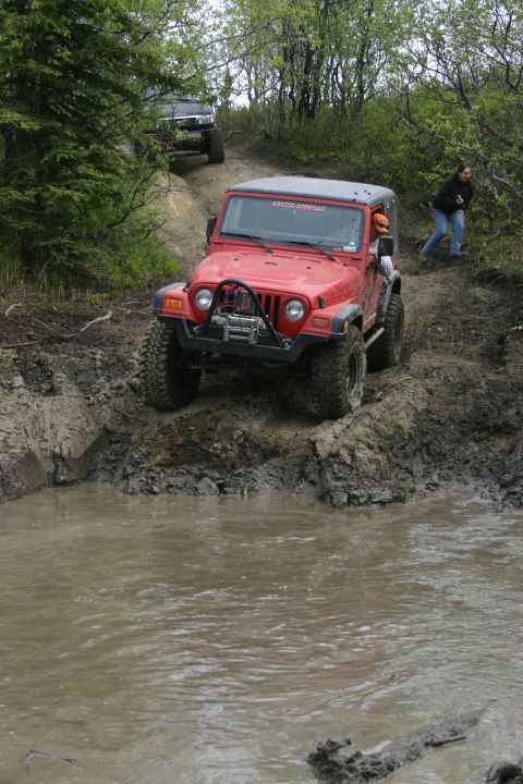 2003 Jeep TJ - Two off-road vehicles navigate a muddy trail with trees on either side.