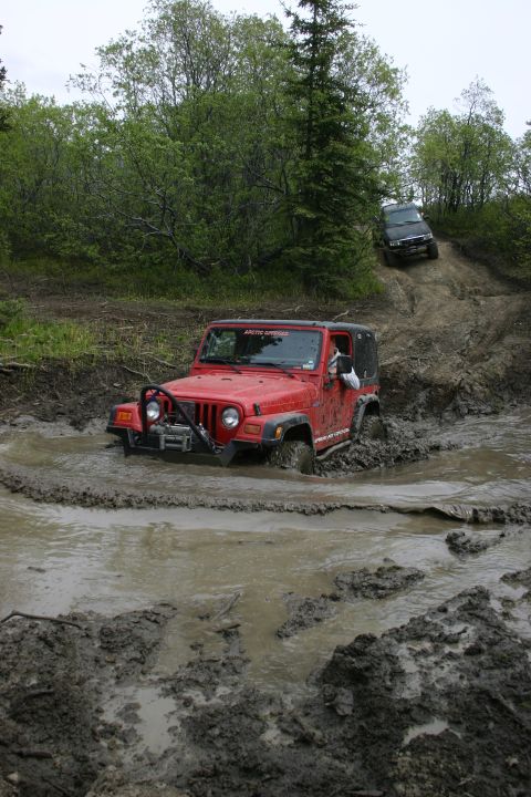 2003 Jeep TJ - Two off-road vehicles navigate a challenging muddy terrain during an outdoor meet and greet event.