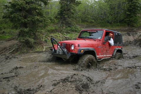 2003 Jeep TJ - Driver navigates a challenging muddy obstacle in a red Jeep TJ Wrangler.