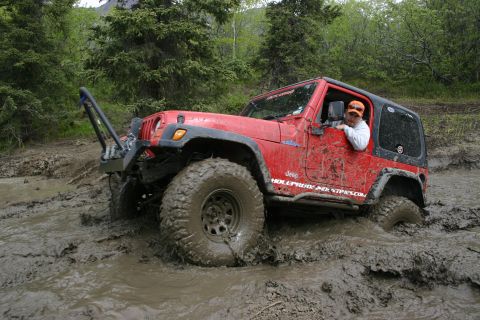 2003 Jeep TJ - A red Jeep Wrangler navigates a muddy trail, with its tires deep in the muck.