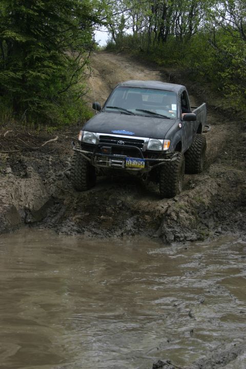 2003 Jeep TJ - A black Toyota Tacoma tackles a challenging muddy off-road course, demonstrating its capabilities.