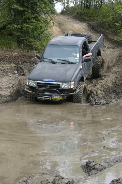 2003 Jeep TJ - Toyota Tacoma navigates a muddy off-road trail, kicking up water and mud.
