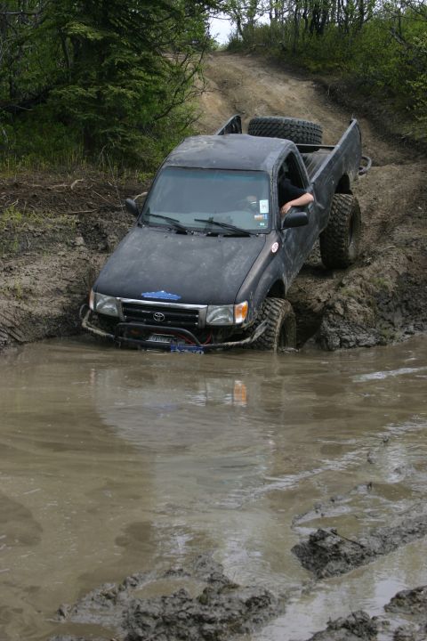 2003 Jeep TJ - This truck is navigating a challenging muddy terrain, with its tires submerged in the mire.