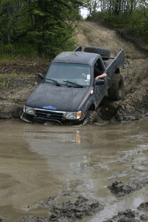 2003 Jeep TJ - A black pickup truck navigates a muddy trail, with its front end deep in the water.