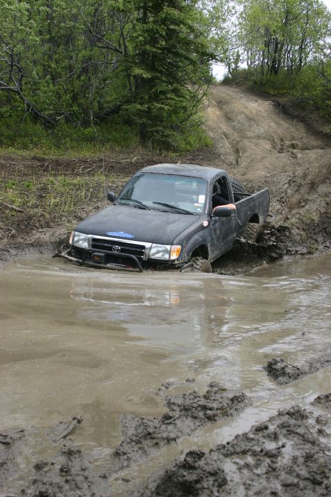 2003 Jeep TJ - A black pickup truck is deeply stuck in a muddy water hole on an off-road trail, wooded trail.