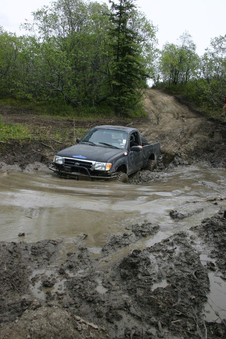 Black Toyota Tacoma stuck in a deep mud puddle on a dirt track
