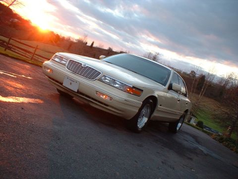 1996 Mercury Grand Marquis - A tan sedan is parked on a wet asphalt surface during sunset with a cloudy sky overhead.
