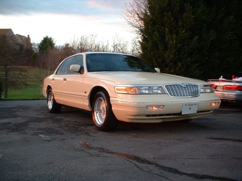 1996 Mercury Grand Marquis - A tan sedan is parked in front of a house with trees and a cloudy sky in the background.