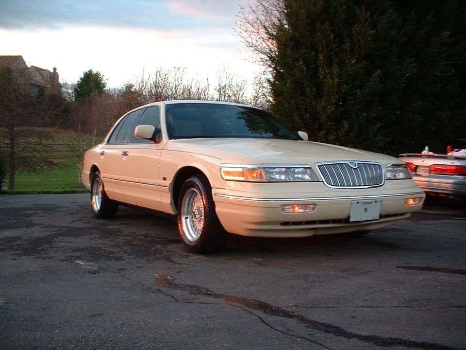 Cream four-door sedan, front-right view, chrome wire wheels, in driveway at dusk