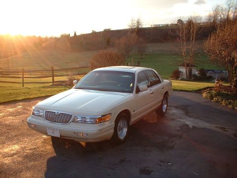 1996 Mercury Grand Marquis - A cream-colored 1995 Mercury Grand Marquis is parked on a wet driveway as the sun sets, casting long shadows.